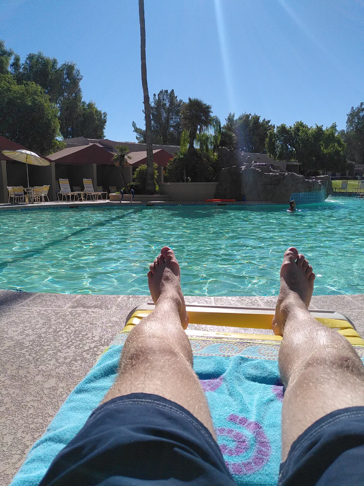 A pair of feet in the foreground with a swimming pool in the background