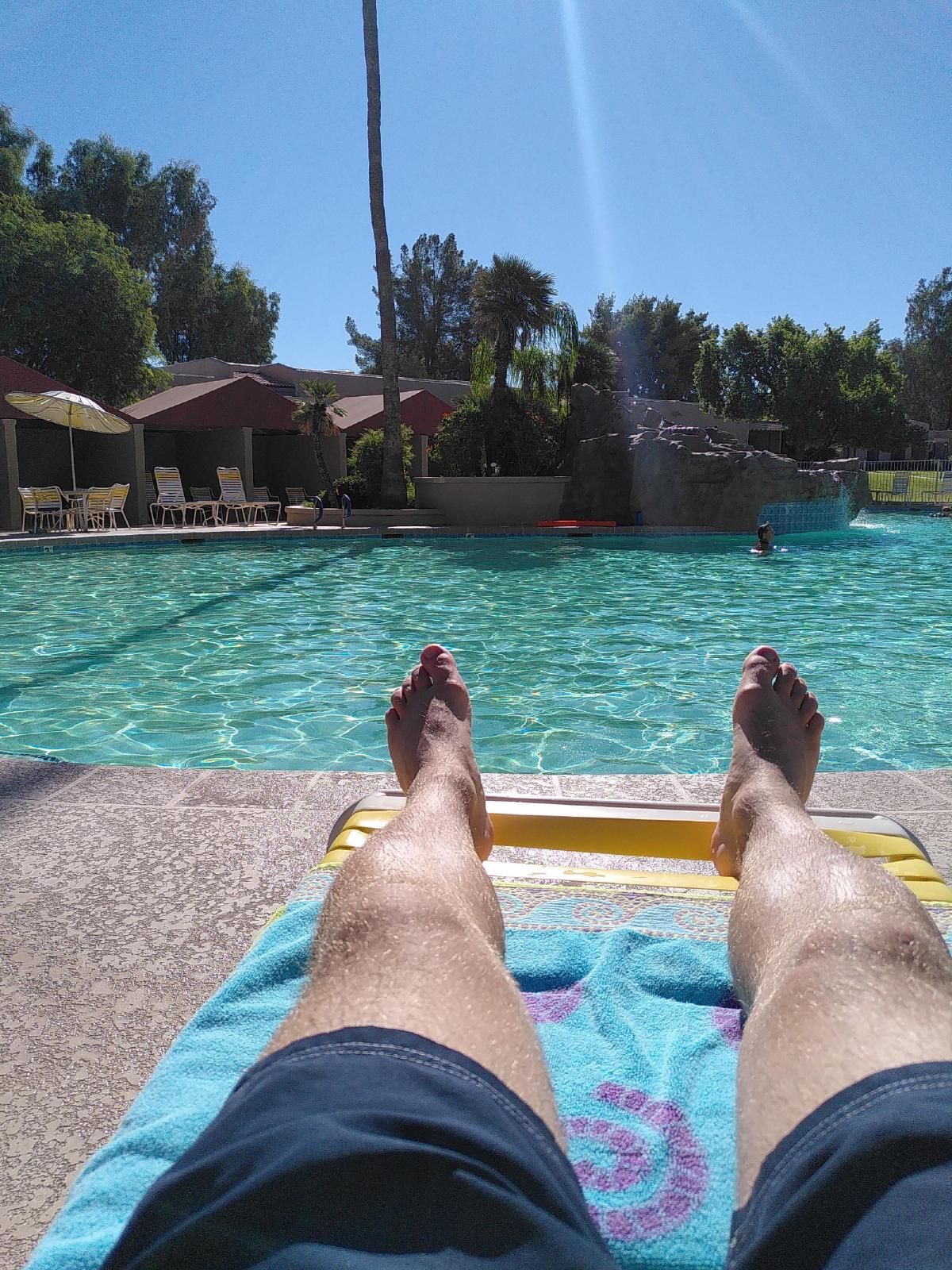 A pair of feet in the foreground with a swimming pool in the background