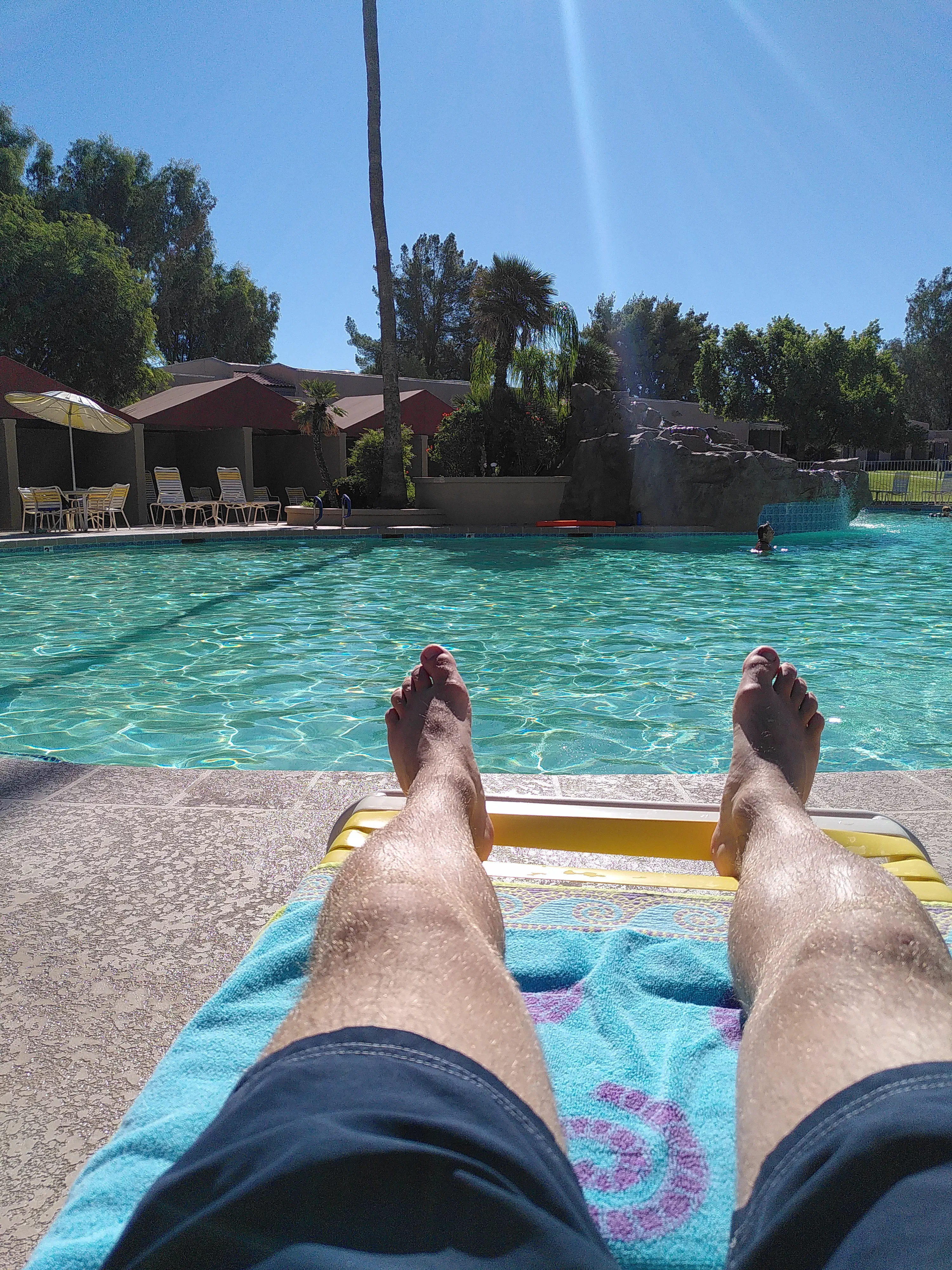 A pair of feet in the foreground with a swimming pool in the background