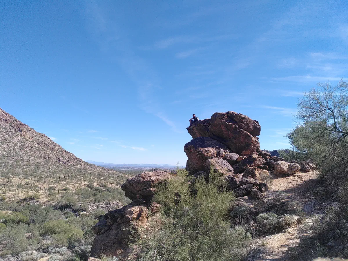 A man sitting on a large rock formation a long distance away