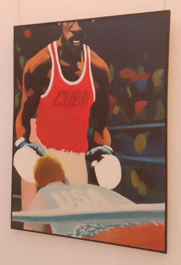 A black boxer wearing a red vest that reads ‘Cuba’ stands triumphant before a white boxer wearing a blue vest that reads ‘USA‘