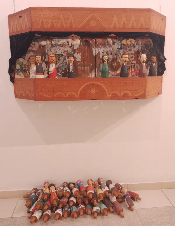 A wall-mounted stage featuring dolls of Che Guevara, Jesus, Charlie Chaplin and more, with a pile of other dolls laying on the floor below it