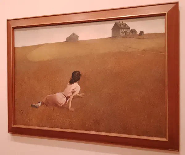 A woman laying in a field looking forwards a distant farmhouse