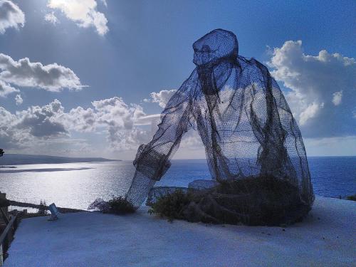 A wireframe statue of a man sat looking out over the Calabrian coastline.