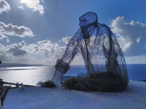 A wireframe statue of a man sat looking out over the Calabrian coastline.