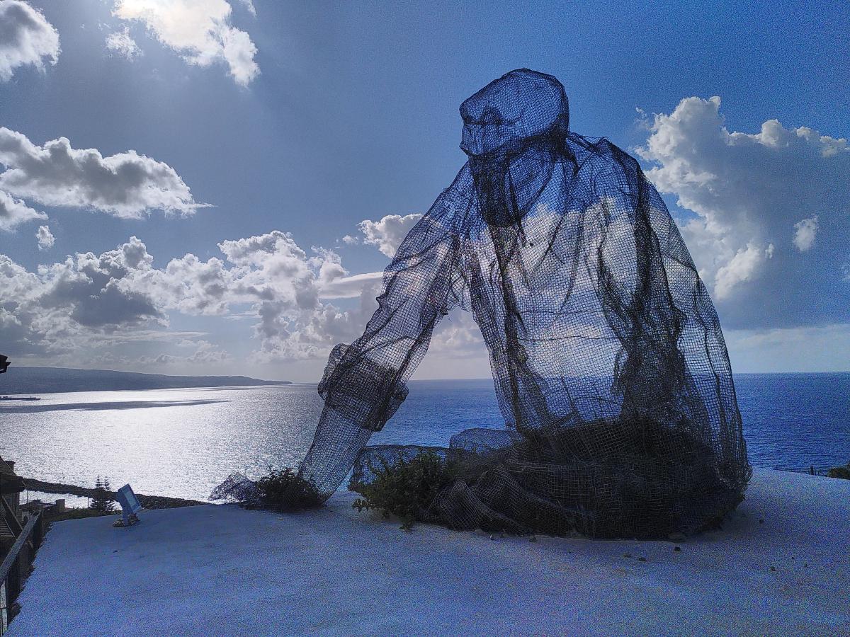 A wireframe statue of a man sat looking out over the Calabrian coastline.