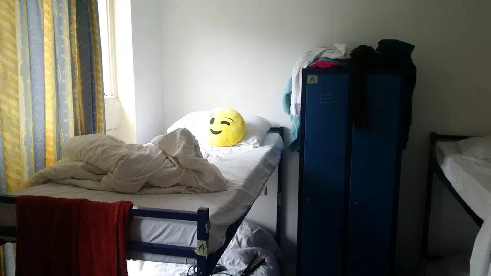 Hostel bunk beds, one of which has an emoji pillow on it