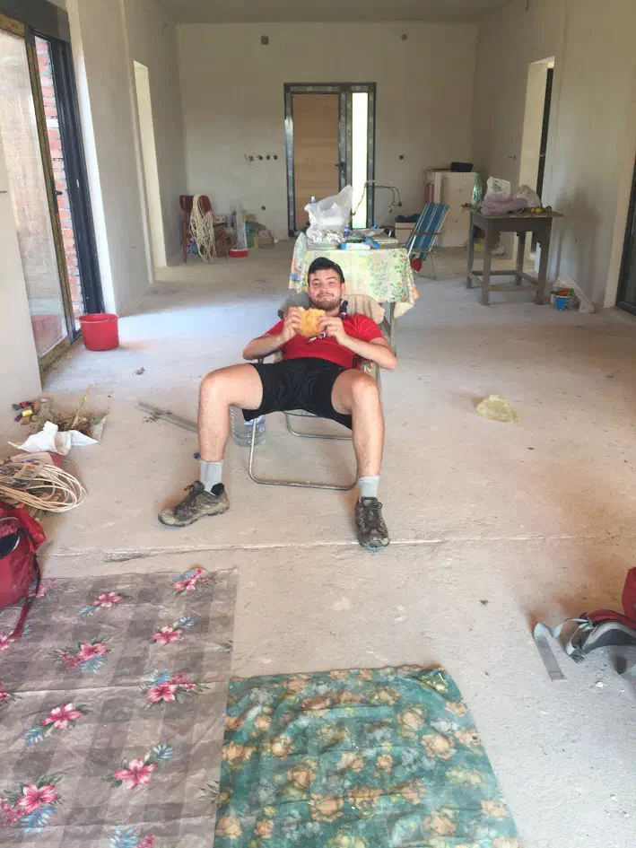 A man reclining inside a construction site, holding a loaf of bread and smiling