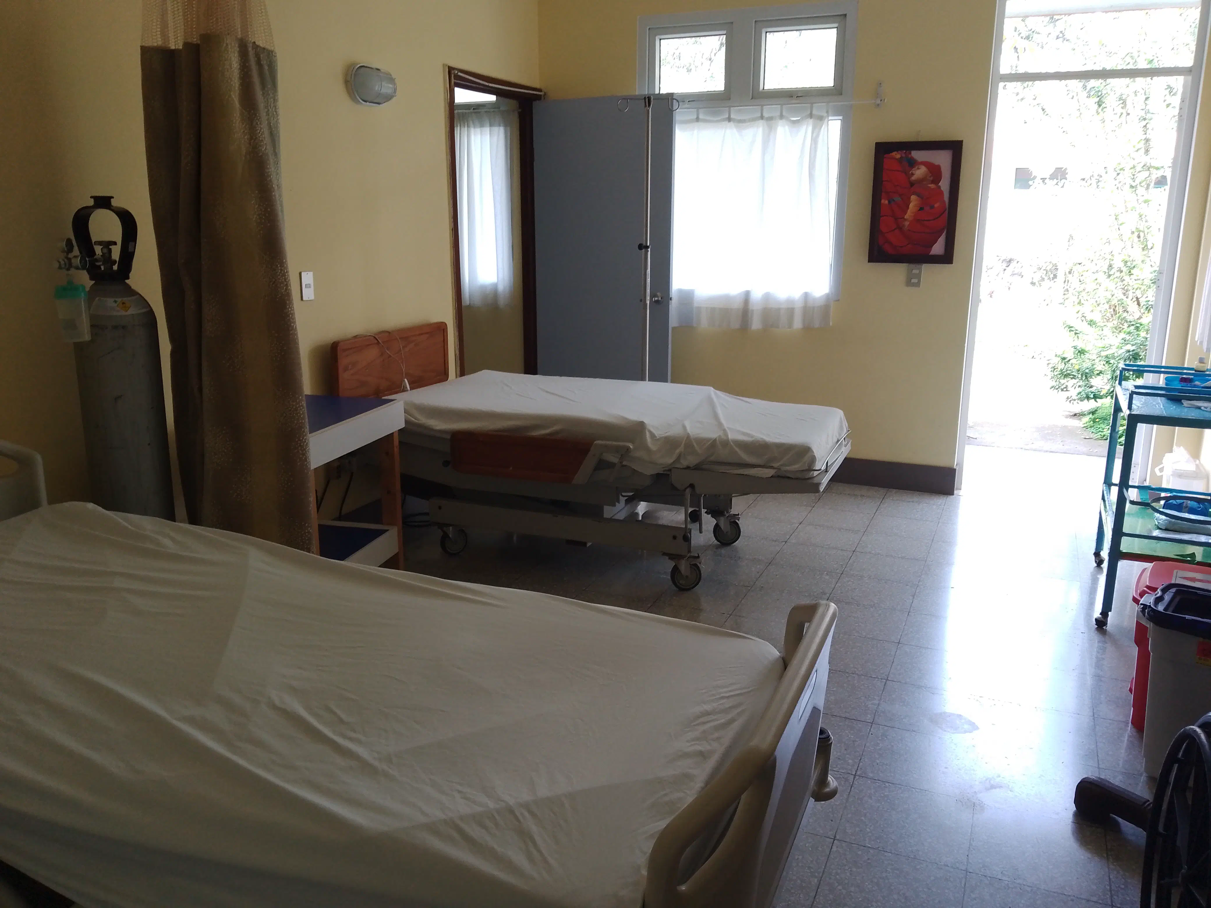 A hospital ward with two beds, some gas cylinders and a door leading to a garden