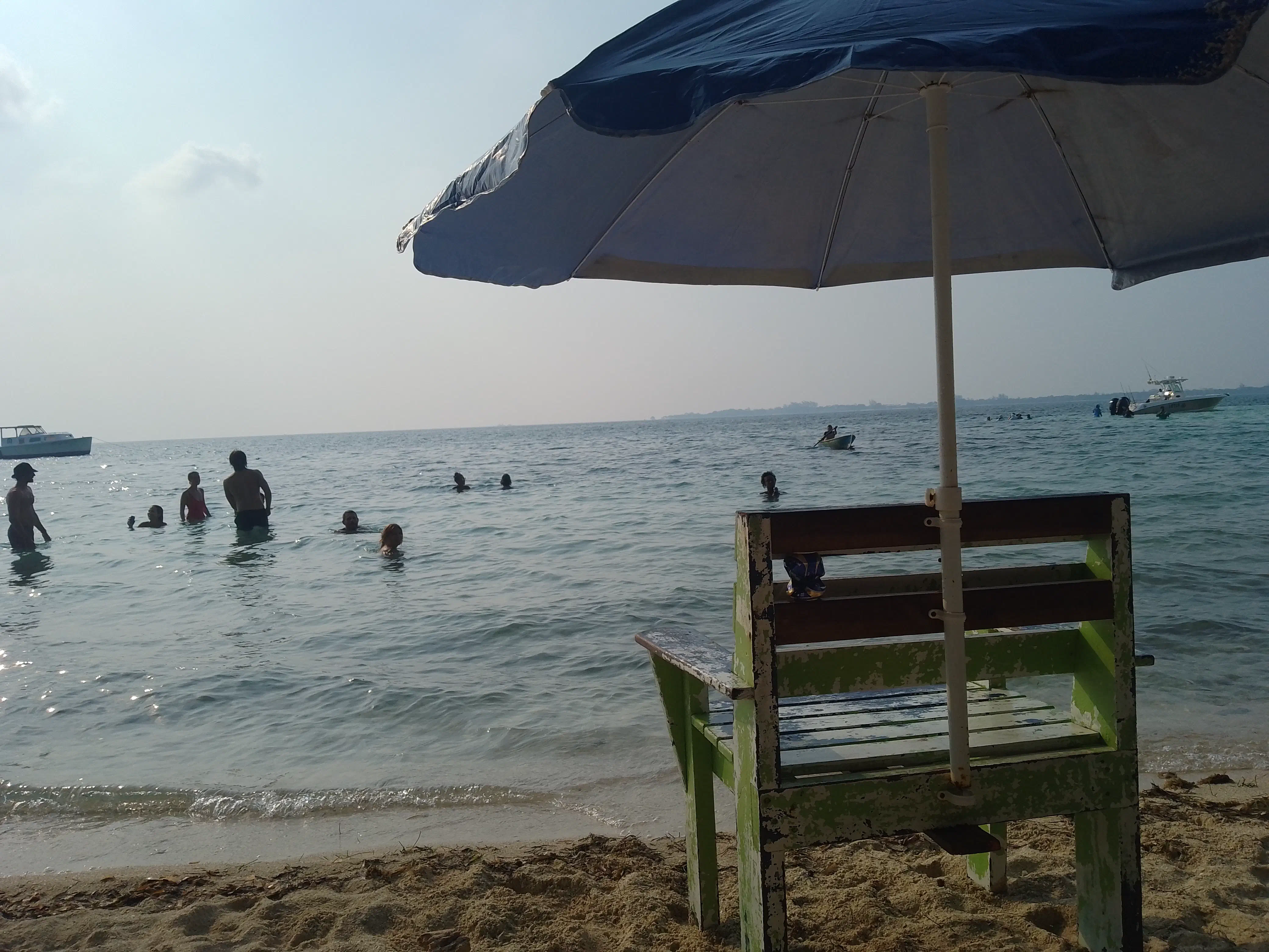 A wooden chair sitting on a beach, looking out over various people playing in the water