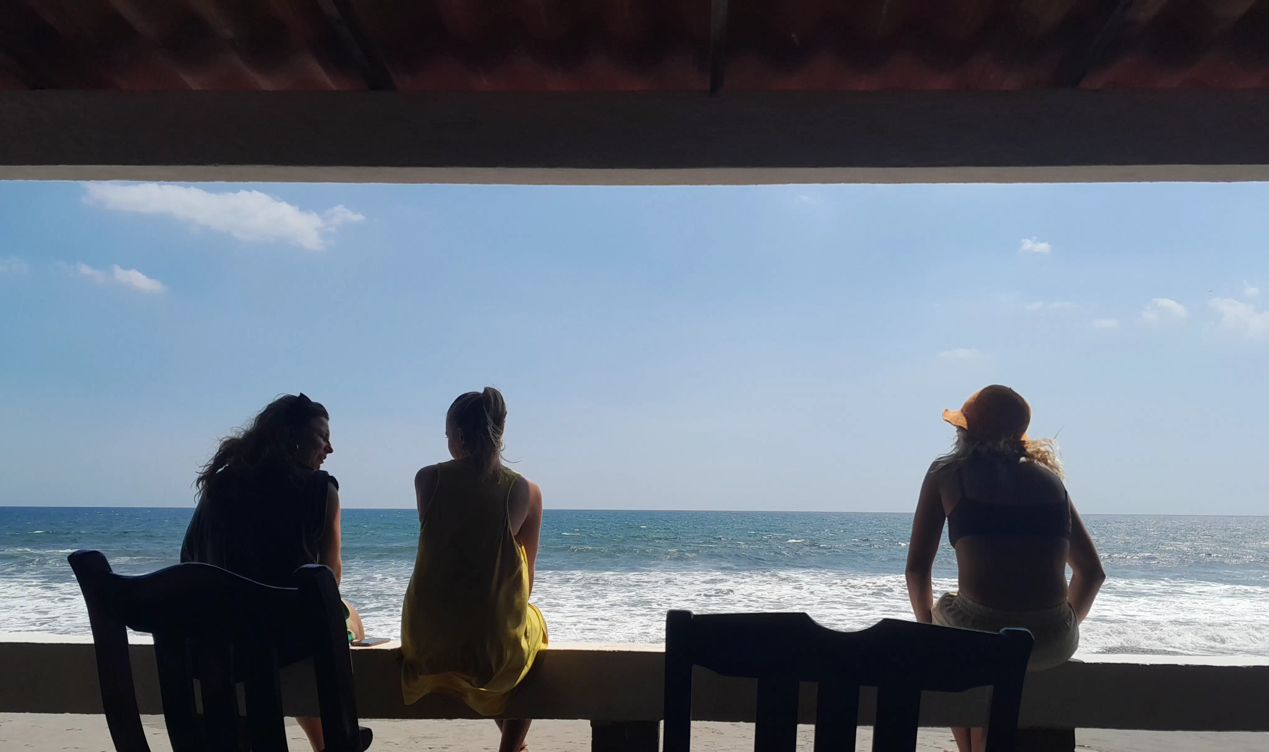 Three women sitting on a bannister, looking out over a beach
