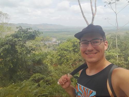 The author in the foreground, resting a machete on his shoulder, with a small village surrounded by jungle in the background