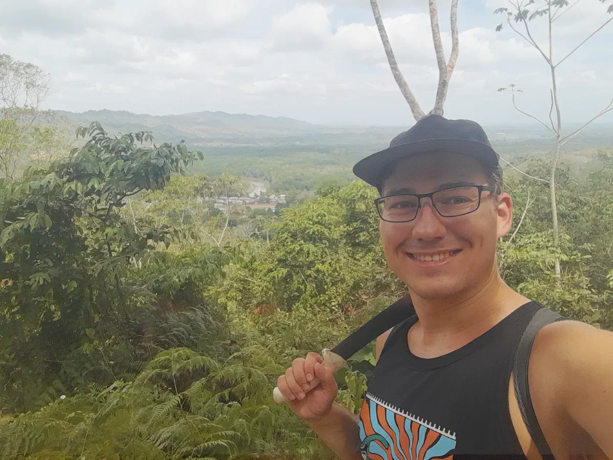 The author in the foreground, resting a machete on his shoulder, with a small village surrounded by jungle in the background