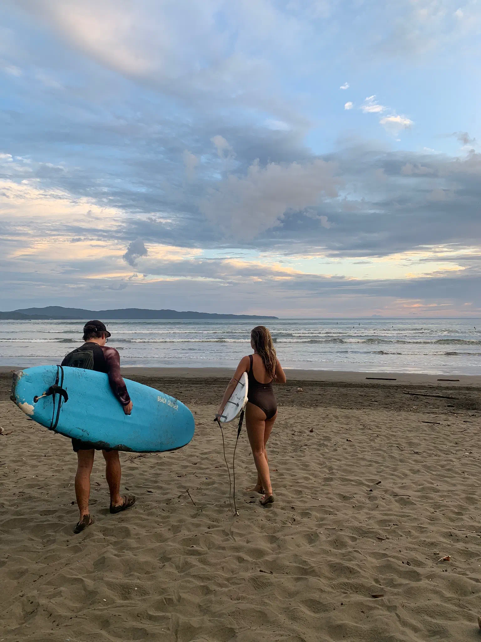 The author and a woman walking toward the sea carrying surfboards