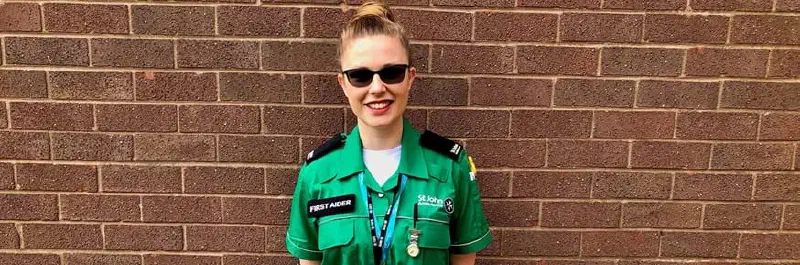 A woman in a St John Ambulance uniform smiling in front of a brick wall