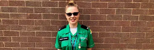 A woman in a St John Ambulance uniform smiling in front of a brick wall