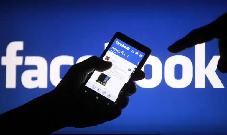 A mobile phone with the Facebook app, in front of a projected Facebook logo