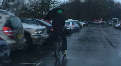 A cyclist riding whilst holding an umbrella