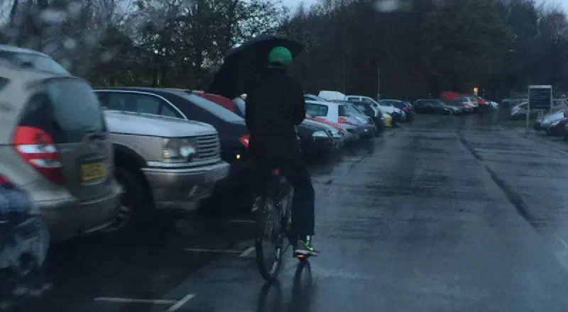 A cyclist riding whilst holding an umbrella