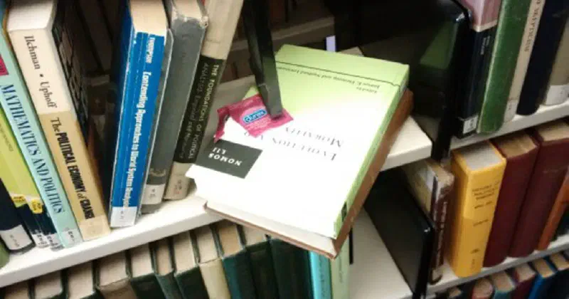 A condom wrapper laying on a book on a library bookshelf