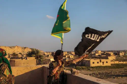 A YPJ fighter replacing a Daesh flag with a YPJ one